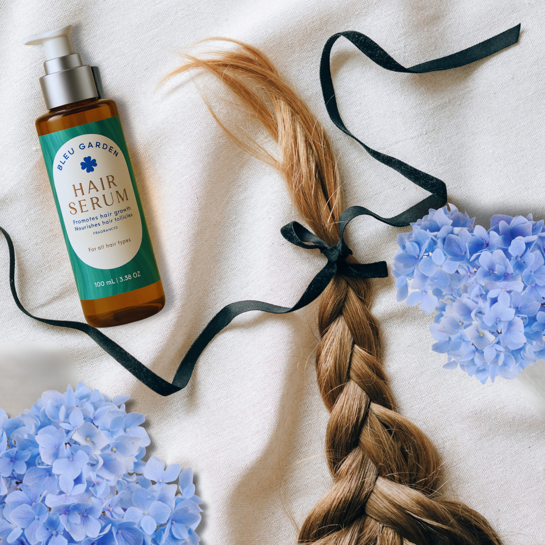 leu Garden Hair Serum bottle on fabric with braided hair, black ribbon, and blue hydrangea flowers – natural haircare product flat lay